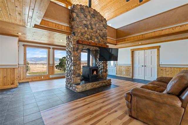 tiled living room featuring wooden walls, a wood stove, wood ceiling, and vaulted ceiling