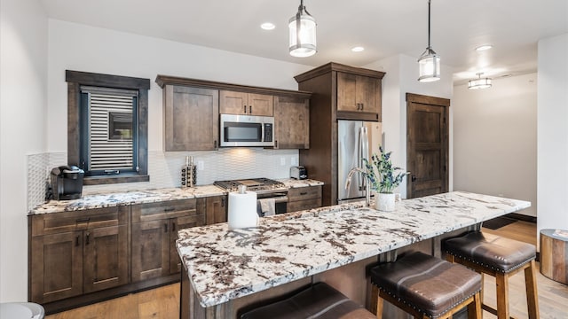 kitchen with light stone countertops, pendant lighting, stainless steel appliances, and light hardwood / wood-style flooring