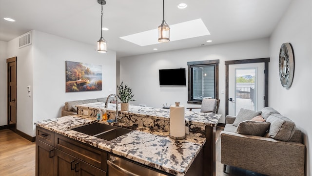 kitchen with sink, a skylight, stainless steel dishwasher, an island with sink, and light hardwood / wood-style floors