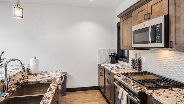 kitchen featuring appliances with stainless steel finishes, tasteful backsplash, light stone counters, sink, and light hardwood / wood-style floors