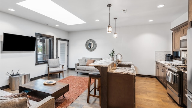 kitchen with light stone countertops, sink, decorative light fixtures, stainless steel range with gas cooktop, and a breakfast bar area