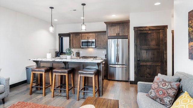 kitchen featuring dark brown cabinetry, stainless steel appliances, pendant lighting, light hardwood / wood-style floors, and an island with sink