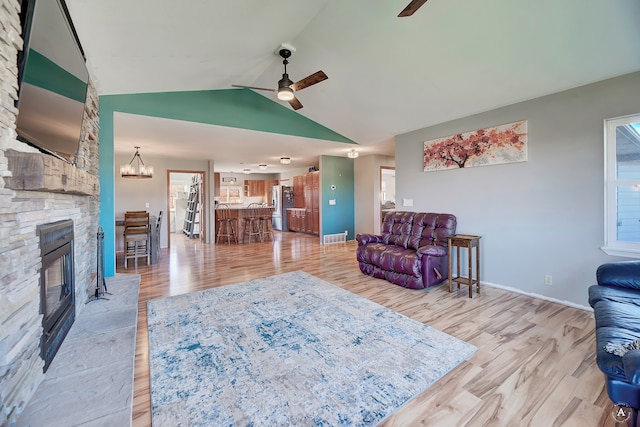 living room with a fireplace, light hardwood / wood-style flooring, ceiling fan with notable chandelier, and vaulted ceiling