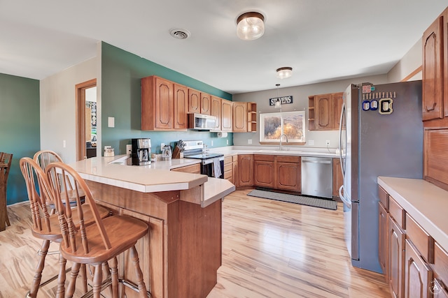 kitchen with sink, stainless steel appliances, light hardwood / wood-style flooring, kitchen peninsula, and a kitchen bar