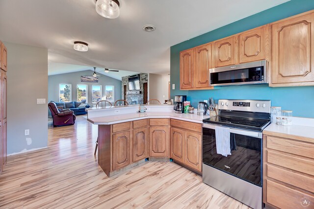 kitchen featuring light wood-type flooring, kitchen peninsula, appliances with stainless steel finishes, and vaulted ceiling