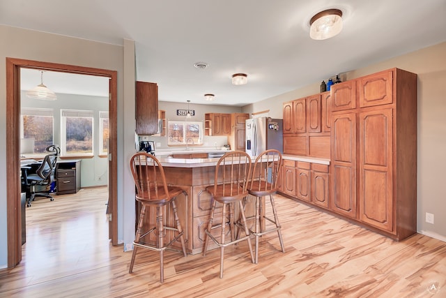 kitchen featuring a kitchen breakfast bar, hanging light fixtures, light wood-type flooring, a kitchen island, and stainless steel fridge with ice dispenser