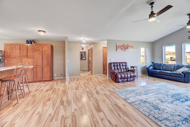 living room featuring ceiling fan, light hardwood / wood-style floors, bar, and vaulted ceiling