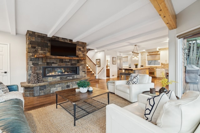 living room featuring beam ceiling, a stone fireplace, and light hardwood / wood-style floors