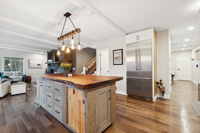 kitchen with wood counters, built in refrigerator, dark hardwood / wood-style floors, beamed ceiling, and a kitchen island