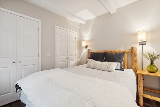 bedroom featuring beam ceiling, multiple closets, and dark hardwood / wood-style floors