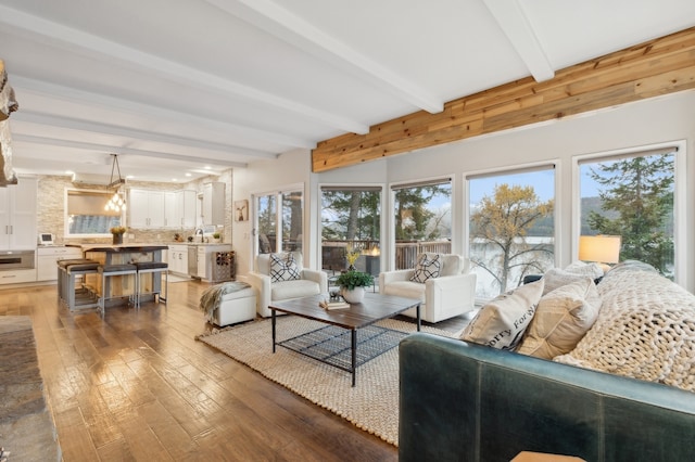 living room featuring sink, an inviting chandelier, beamed ceiling, and hardwood / wood-style flooring