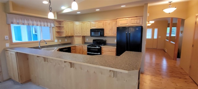 kitchen featuring kitchen peninsula, a kitchen bar, sink, black appliances, and decorative light fixtures