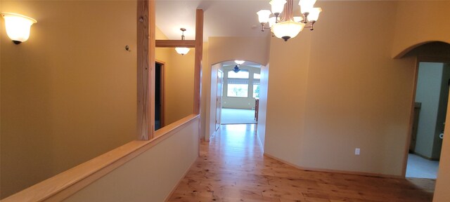 hall with light wood finished floors, baseboards, arched walkways, and a chandelier