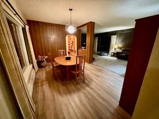 dining room with a textured ceiling, hardwood / wood-style flooring, and wooden walls