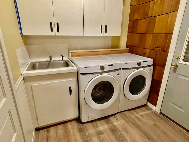 clothes washing area with light hardwood / wood-style floors, cabinets, sink, and washing machine and clothes dryer