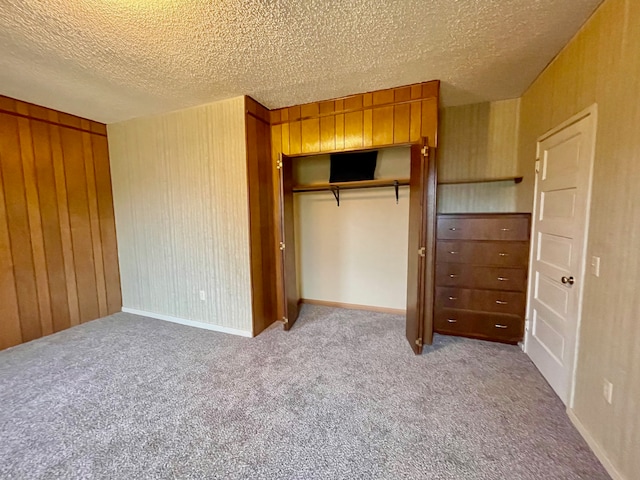 unfurnished bedroom featuring a textured ceiling, light colored carpet, a closet, and wooden walls