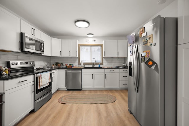 121 Mill Ave, Whitefish, MT 59937 - kitchen featuring stainless steel appliances, dark countertops, light wood-style flooring, decorative backsplash, and white cabinetry