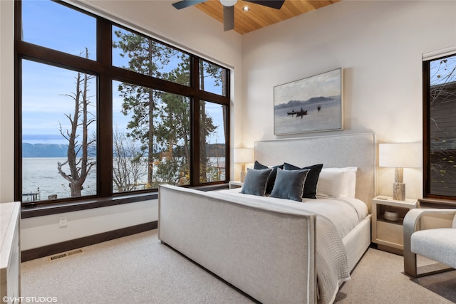 carpeted bedroom featuring a water view, multiple windows, and wood ceiling