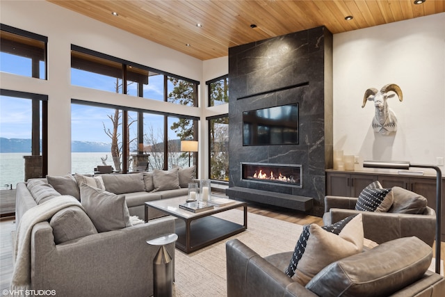 living room with a healthy amount of sunlight, a high end fireplace, wood ceiling, and light wood-type flooring