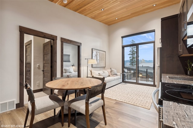 dining space featuring a towering ceiling, light hardwood / wood-style floors, and wood ceiling