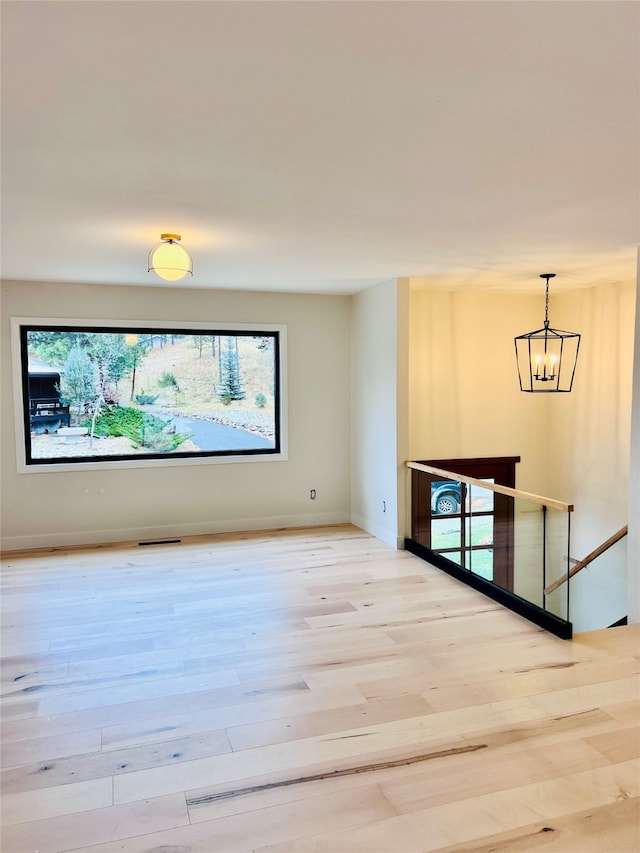 unfurnished room with a notable chandelier, plenty of natural light, and light hardwood / wood-style flooring