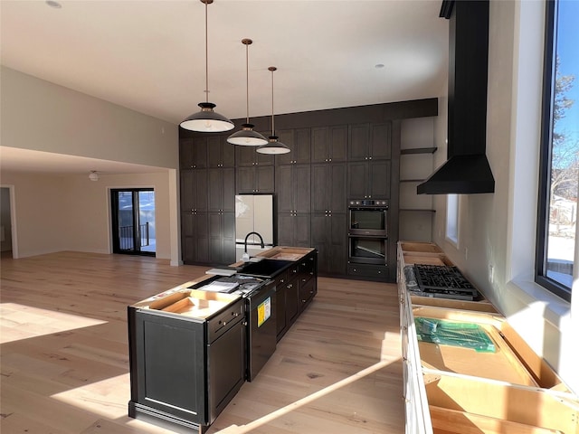 kitchen featuring a kitchen island with sink, fridge, wall chimney exhaust hood, and light wood-type flooring