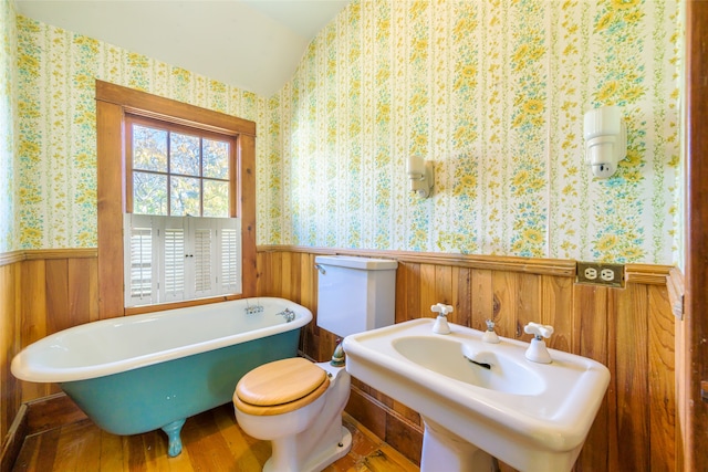 bathroom featuring a washtub, sink, hardwood / wood-style floors, toilet, and wood walls