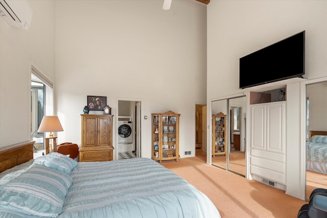 bedroom featuring light carpet, a towering ceiling, a wall unit AC, washer / dryer, and a closet