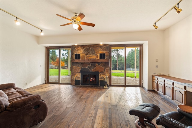 living room featuring hardwood / wood-style flooring, ceiling fan, a stone fireplace, and rail lighting