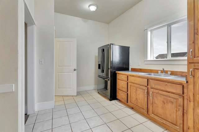 kitchen featuring black refrigerator with ice dispenser, sink, and light tile patterned floors