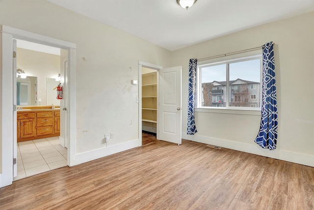 unfurnished bedroom with ensuite bathroom, a walk in closet, light wood-type flooring, and a closet