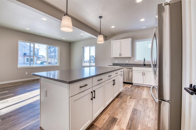 kitchen featuring pendant lighting, stainless steel appliances, a center island, light hardwood / wood-style floors, and white cabinets