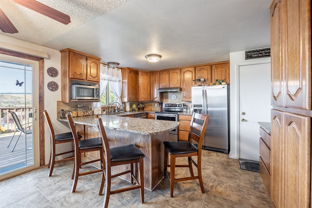 kitchen with light stone countertops, sink, stainless steel appliances, a kitchen breakfast bar, and a textured ceiling