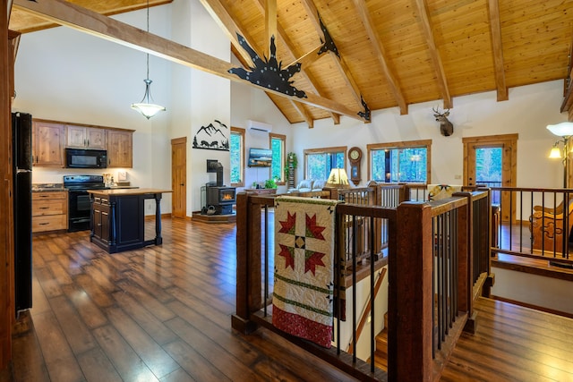 interior space featuring a center island, a wood stove, dark wood-type flooring, high vaulted ceiling, and black appliances