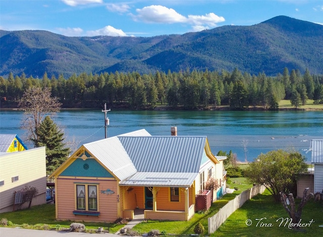 exterior space featuring metal roof, fence, a front lawn, and a water and mountain view