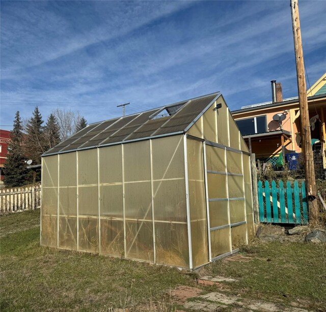 view of greenhouse featuring fence and a lawn