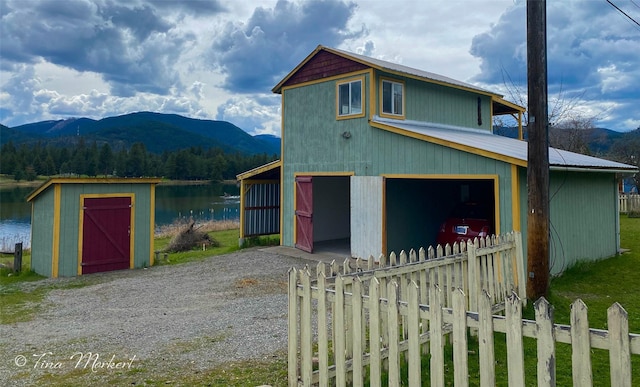 view of front of house featuring a garage, fence, a water and mountain view, and an outbuilding