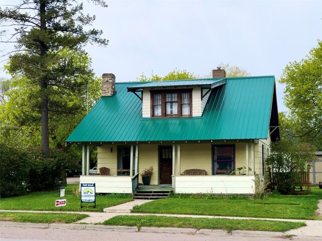508 1st St W, Polson, MT 59860 - view of front of house featuring a chimney, a porch, metal roof, and a front lawn