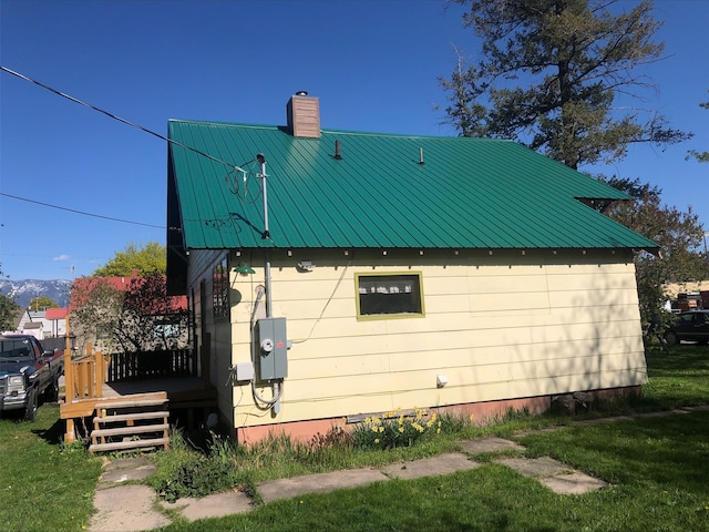 508 1st St W, Polson, MT 59860 - view of side of home featuring a chimney, a deck, metal roof, and a yard