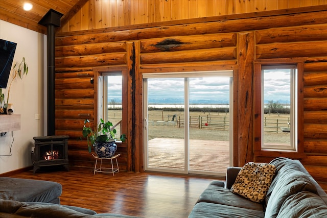 living room with a wealth of natural light, log walls, dark hardwood / wood-style floors, a wood stove, and lofted ceiling