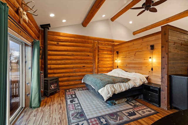 bedroom with ceiling fan, log walls, beam ceiling, hardwood / wood-style floors, and a wood stove