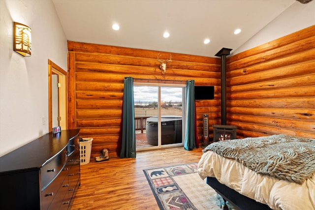 bedroom featuring access to exterior, rustic walls, light hardwood / wood-style floors, a wood stove, and lofted ceiling