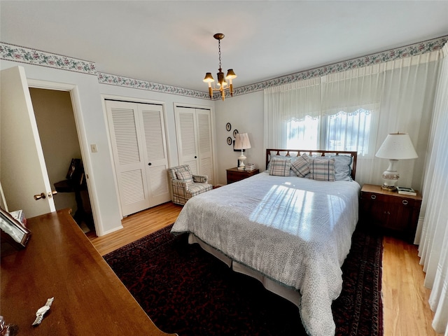 bedroom featuring wood-type flooring, two closets, and an inviting chandelier