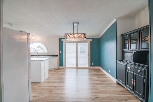 unfurnished dining area with a textured ceiling, ornamental molding, light hardwood / wood-style floors, and a chandelier