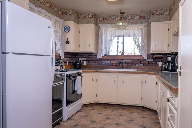 kitchen with white appliances, white cabinetry, hanging light fixtures, and sink