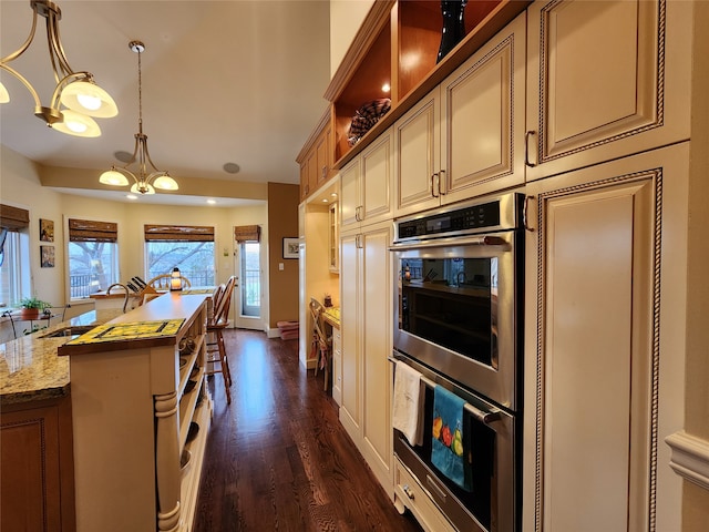 kitchen featuring hanging light fixtures, dark hardwood / wood-style floors, light stone countertops, double oven, and a chandelier