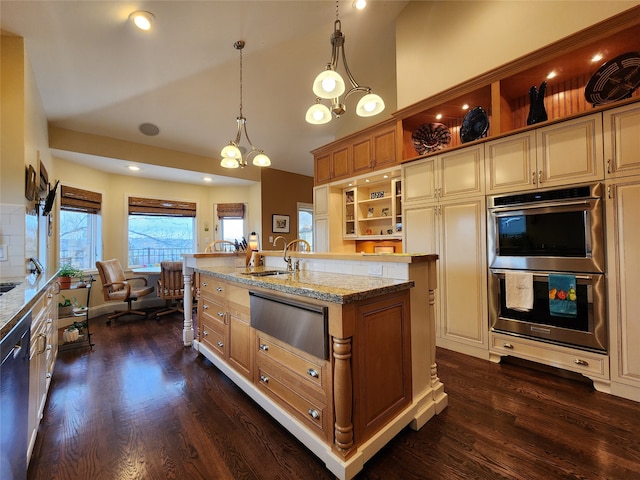 kitchen featuring dark wood-type flooring, hanging light fixtures, a notable chandelier, double oven, and a center island with sink