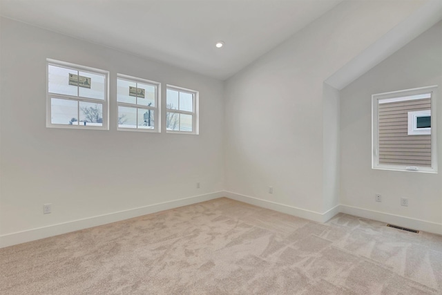 unfurnished room featuring light colored carpet, visible vents, vaulted ceiling, and baseboards