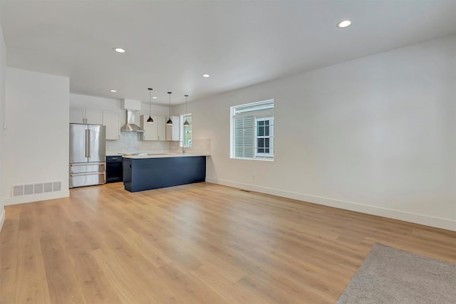 kitchen with wall chimney exhaust hood, high quality fridge, open floor plan, light countertops, and light wood-style floors