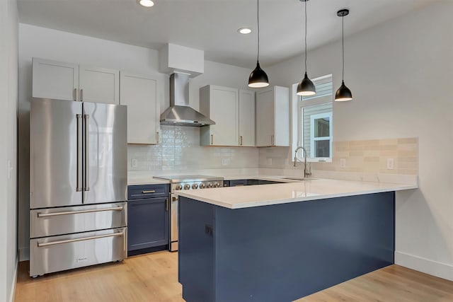 kitchen featuring stainless steel appliances, light countertops, a sink, wall chimney range hood, and a peninsula